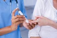 Mid section of doctor examining pregnant woman's blood sugar